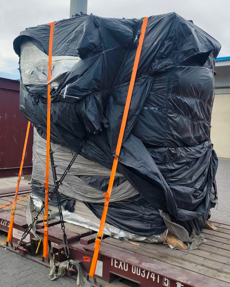 Machinery wrapped in protective sheeting and secured with ratchet straps on a flat rack