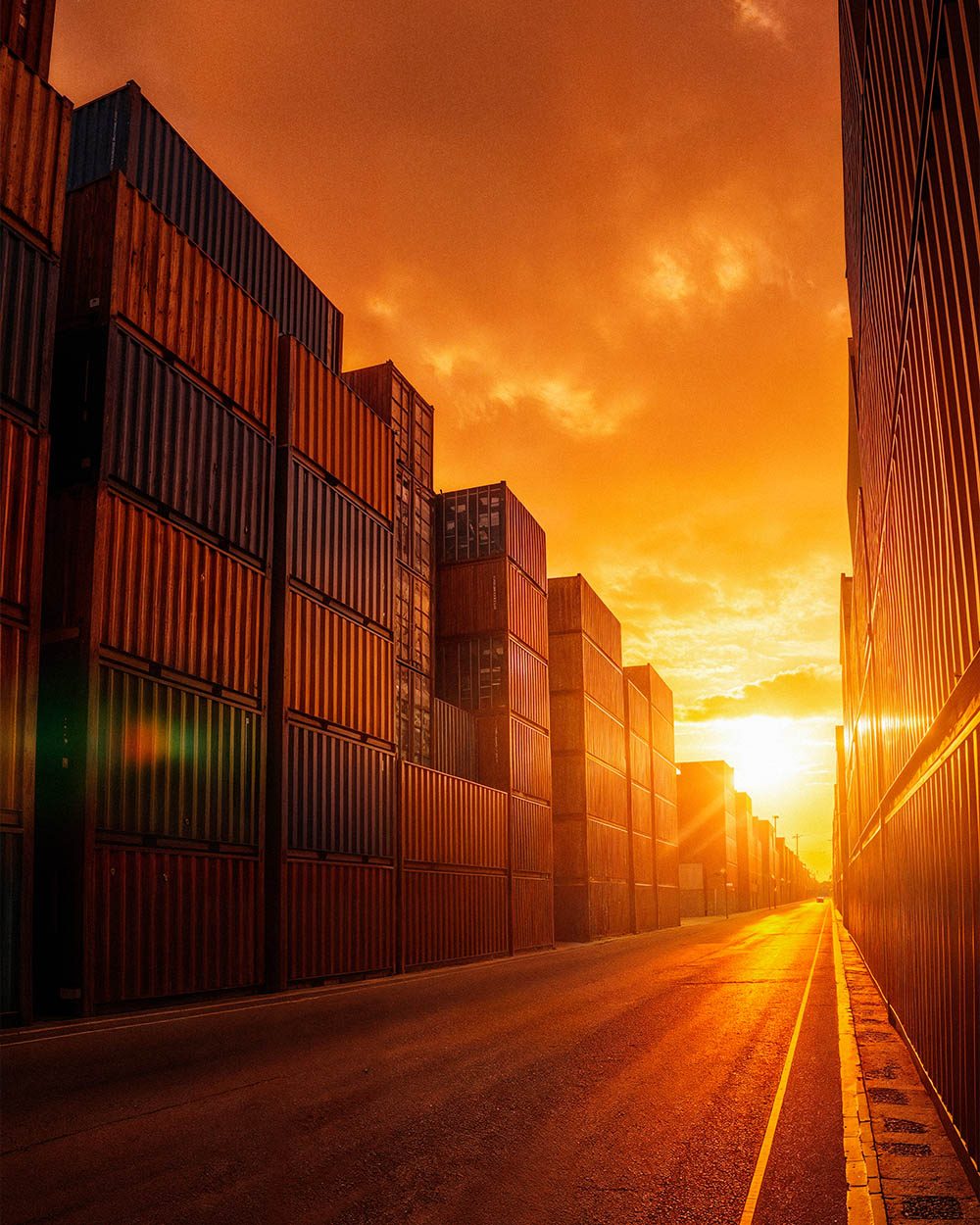 Stacked shipping containers lining a container-yard road at sunset